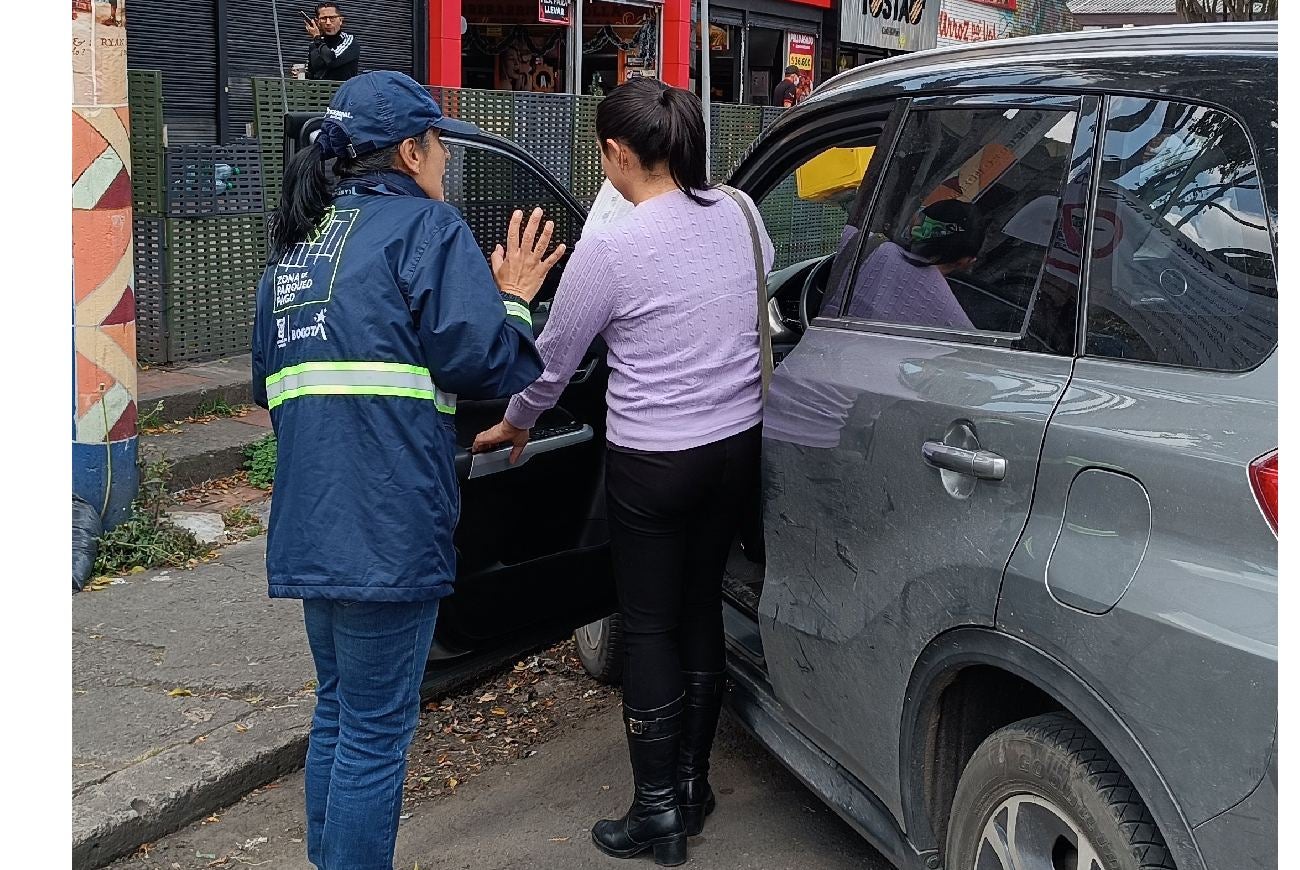 Mujer cuidadora de zonas de parqueo hablándole a una conductora