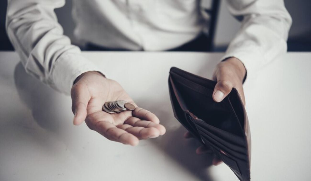 Hombre mirando su billetera vacía y contando monedas