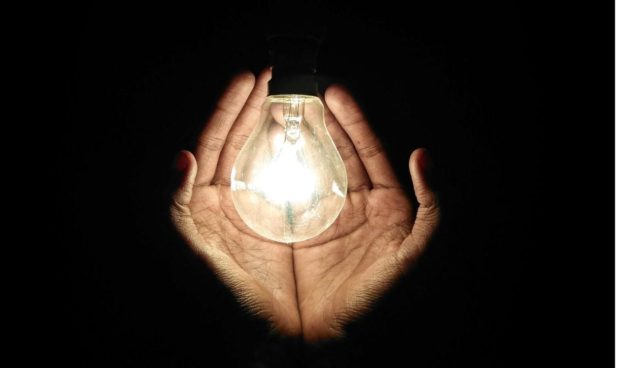 Manos sosteniendo un bombillo en un fondo oscuro