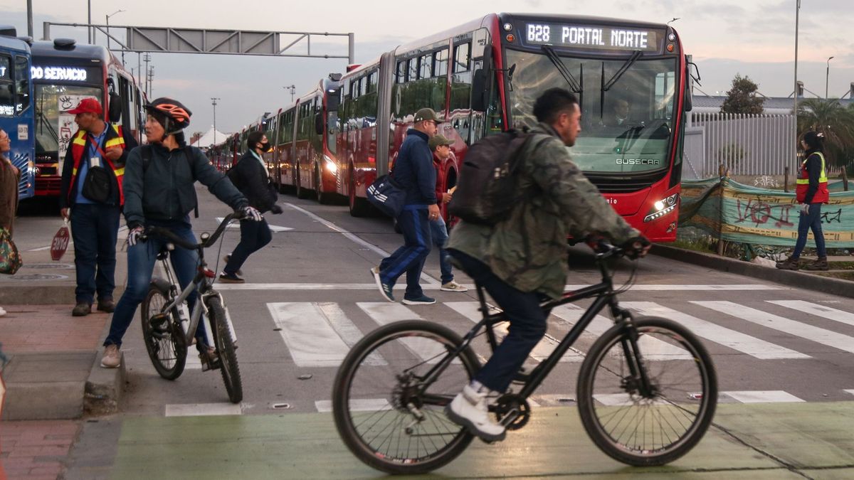 Ciudadanos en bicicleta cruzando una troncal de TransMilenio con los buses de fondo