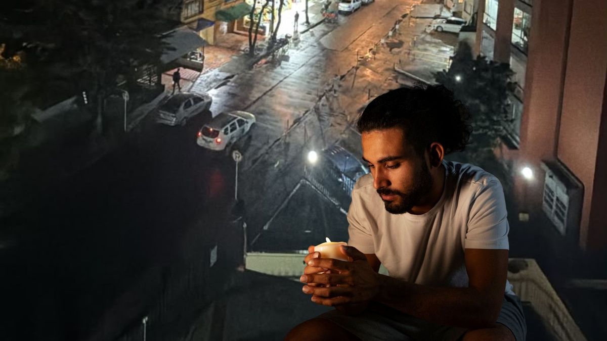 Barrio sin luz y hombre alumbrando con una vela